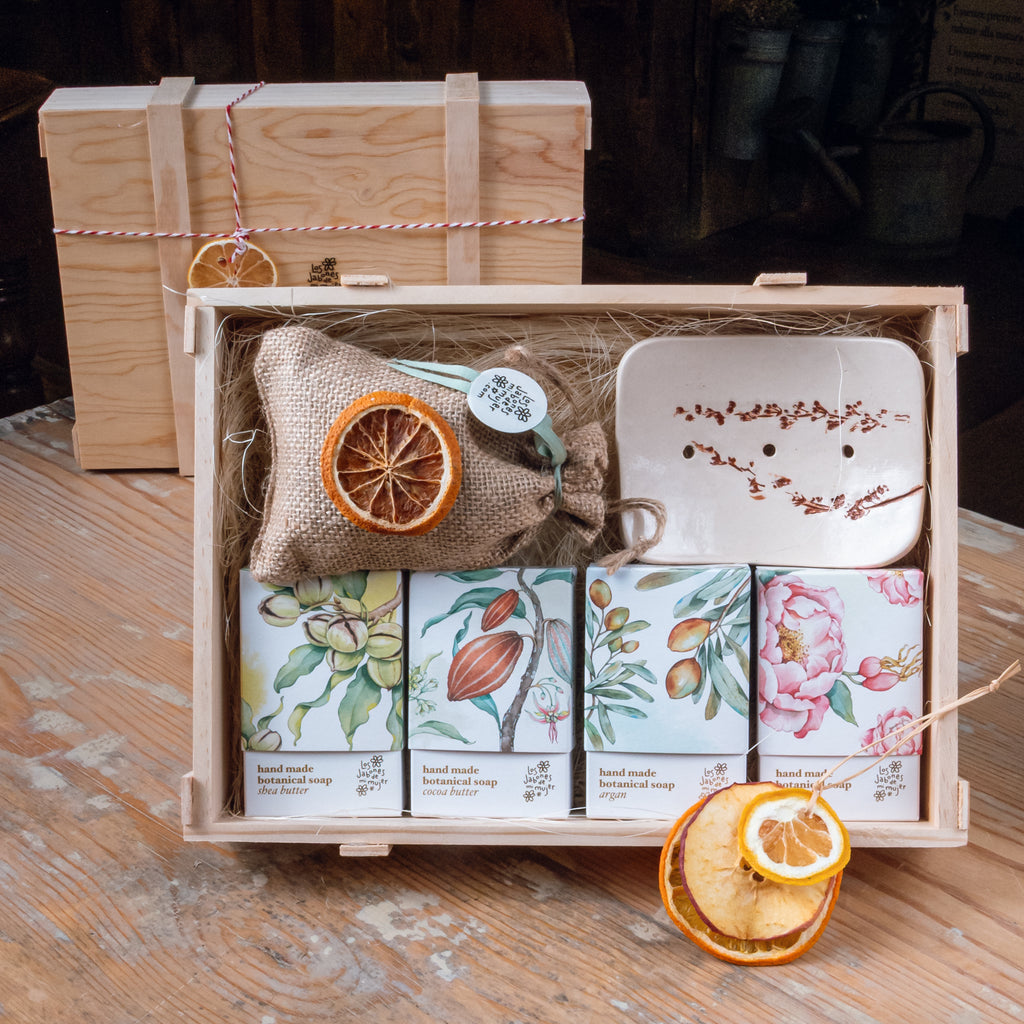 Caja de madera abierta con jabones naturales artesanales, jabonera de cerámica decorada, saquito de lavanda y rodajas de fruta deshidratada como adorno