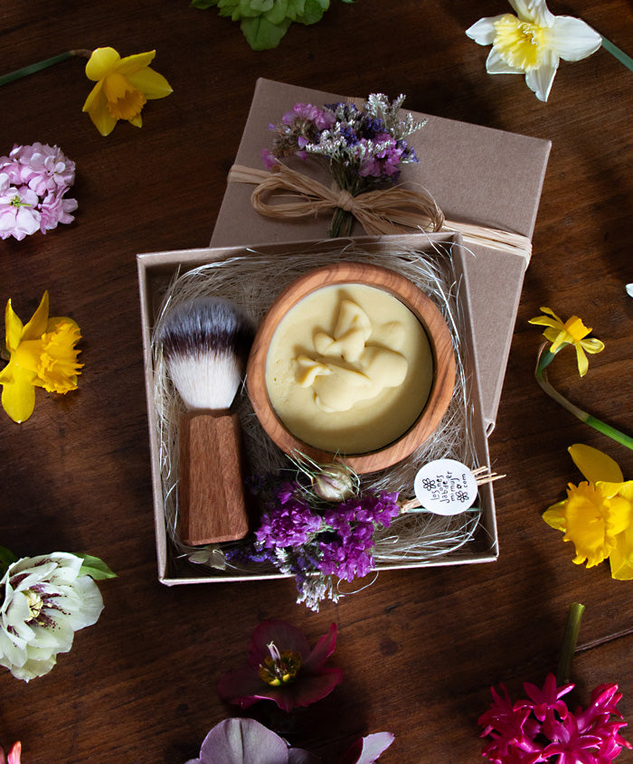 Caja regalo con cuenco y cepillo de olivo para el afeitado rodeado de flores